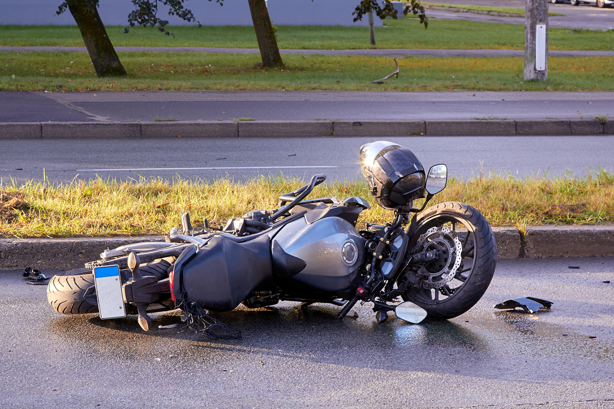 Motorcycle damaged along the curb with a helmet resting on the handlebars.