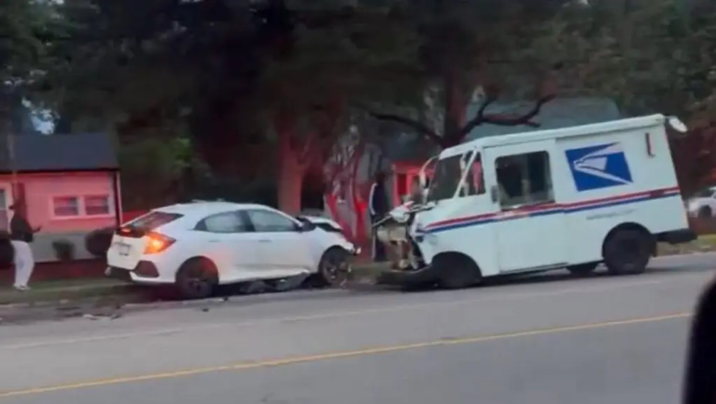 USPS mail truck and white hatchback with front-end damage after a federal vehicle crash on a residential street